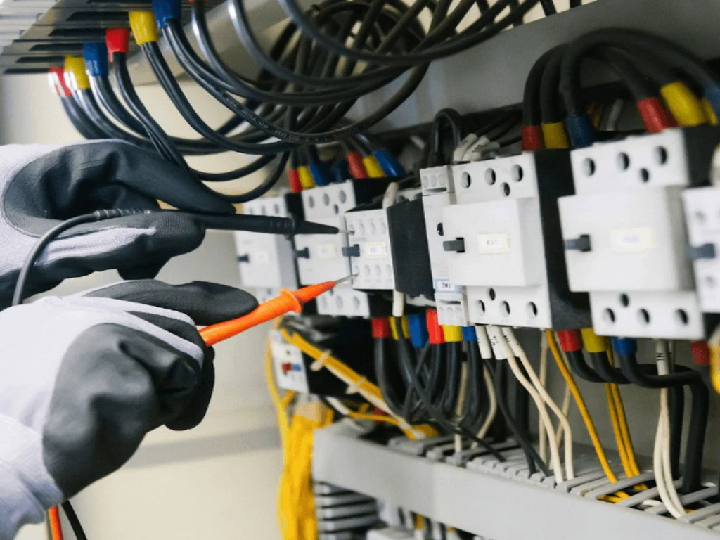 Mano con guanto che verifica un contattore con la sonda di un multimetro